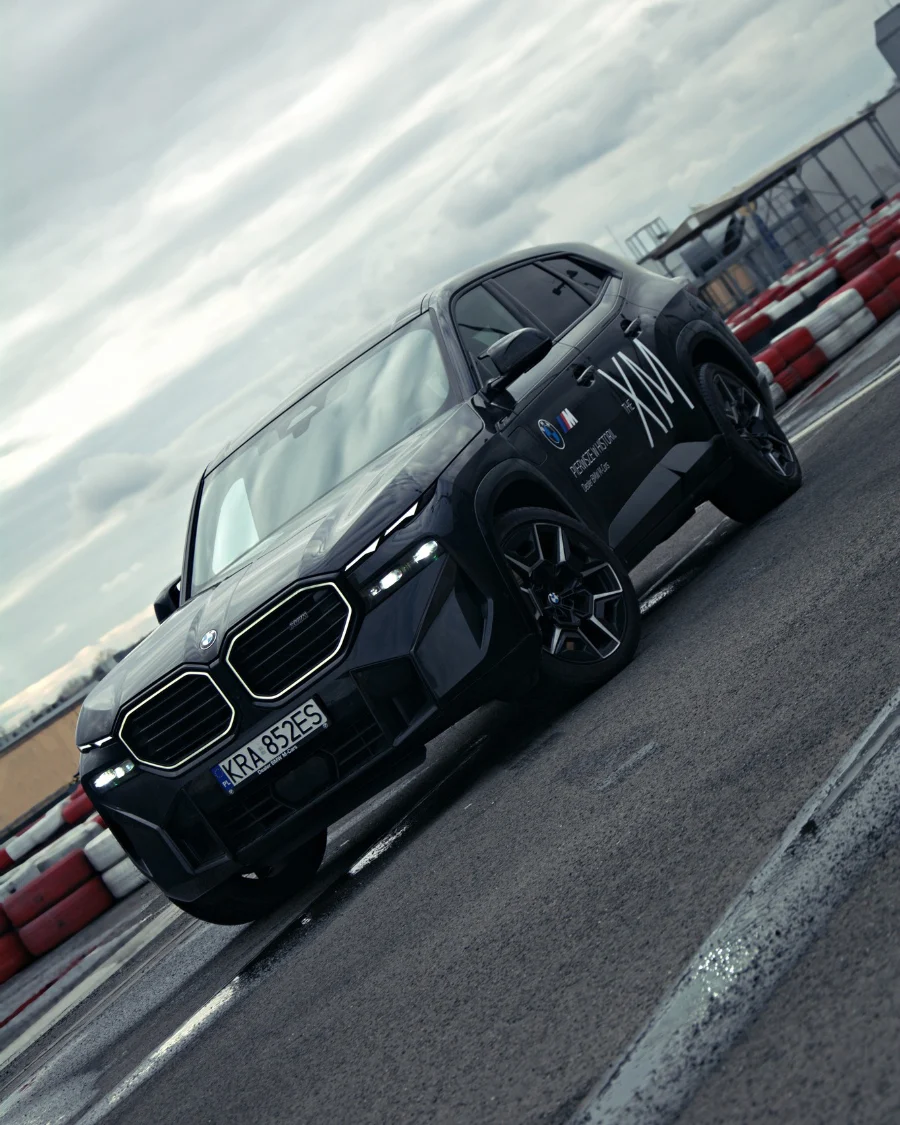 BMW XM ujęcie dynamiczne 3/4 przodu na tle barier torowych