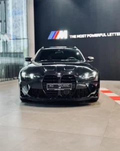 BMW M3 Competition Touring 2026 z przodu w salonie BMW M-Cars, czarny lakier i sportowy pakiet M